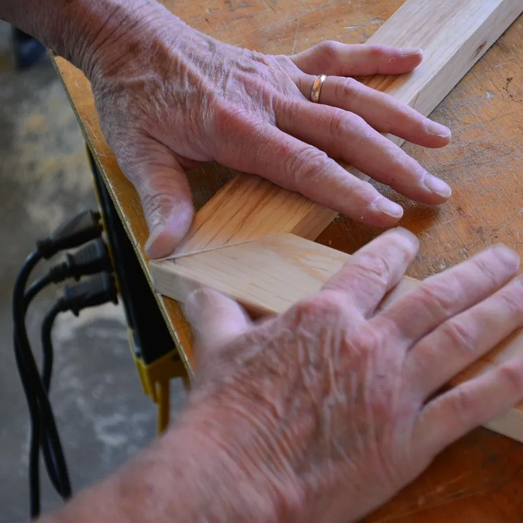 Half-lap joint clamped by hand on a workbench Two hands holding a pine half-lap joint together on a workbench, a no-power-tool joint for a beginner build.