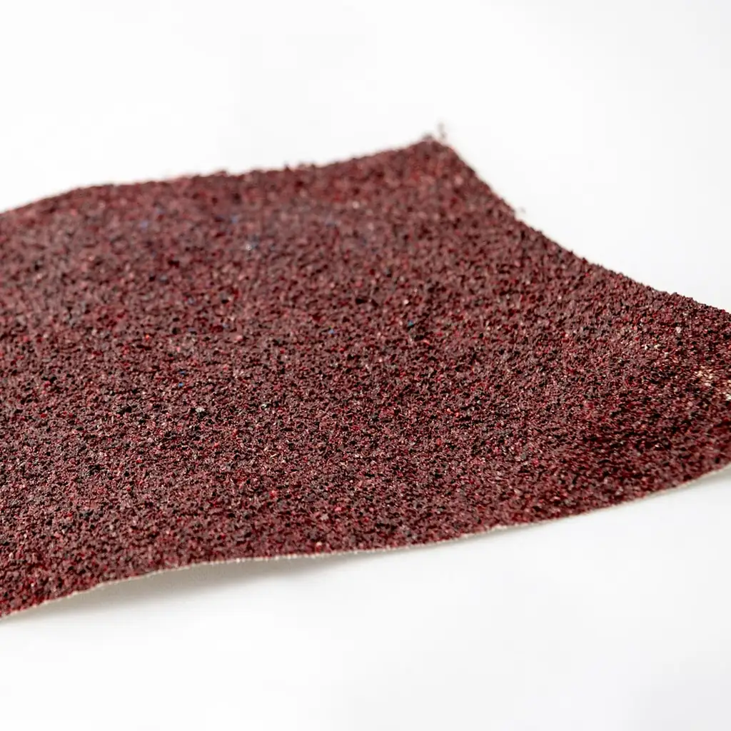 A folded sheet of coarse red abrasive paper on a white background.
