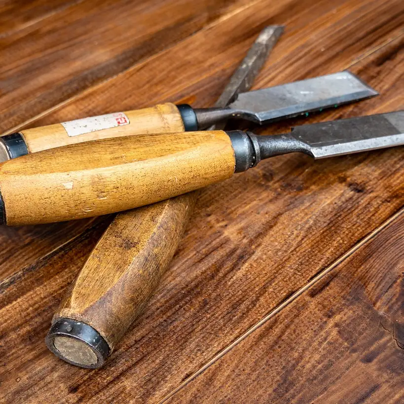 Two wooden-handled bench chisels lying on a dark polished wooden surface.
