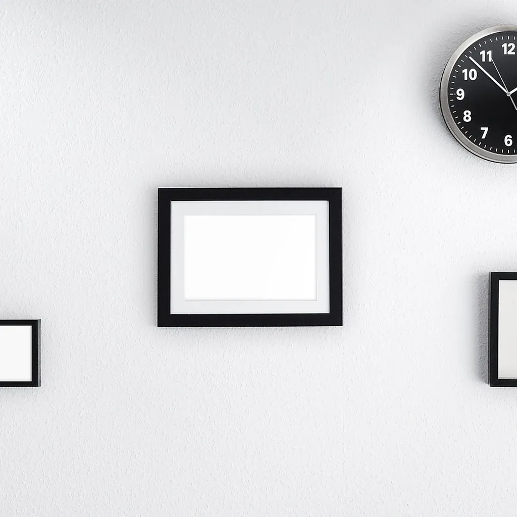 Finished frames hung on a wall Three empty black picture frames of different sizes hung on a white wall beside a round clock.