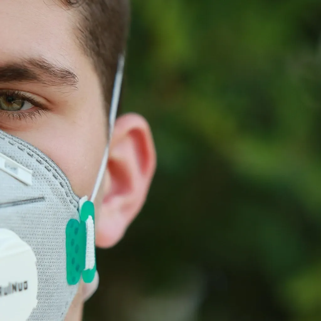 A rated filtering respirator, not a cloth mask A person wearing a moulded white filtering respirator with an exhalation valve.