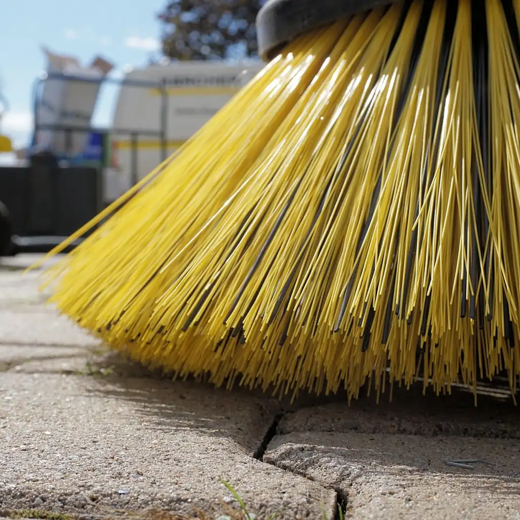 Weekly sweep that keeps dust from accumulating Close-up of the stiff yellow bristles of a sweeping brush resting on a hard floor.