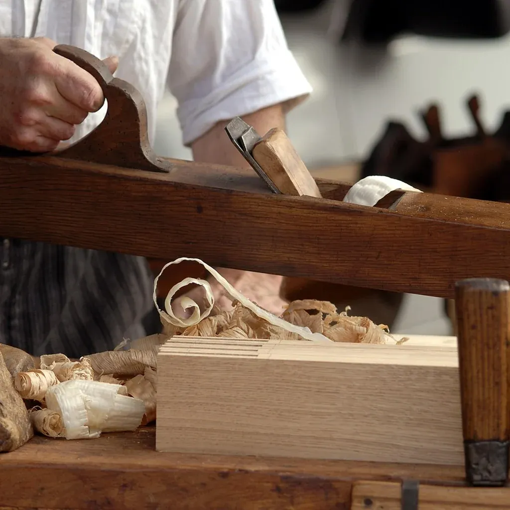 Smoothing a box side with a hand plane A woodworker pushing a hand plane along a board, curled shavings gathering on the bench.