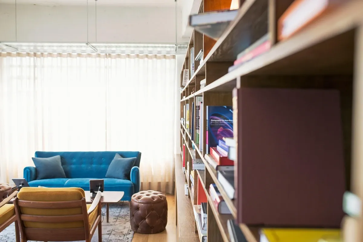 A wall of shelving filled with books in a small living room with a sofa and armchair.