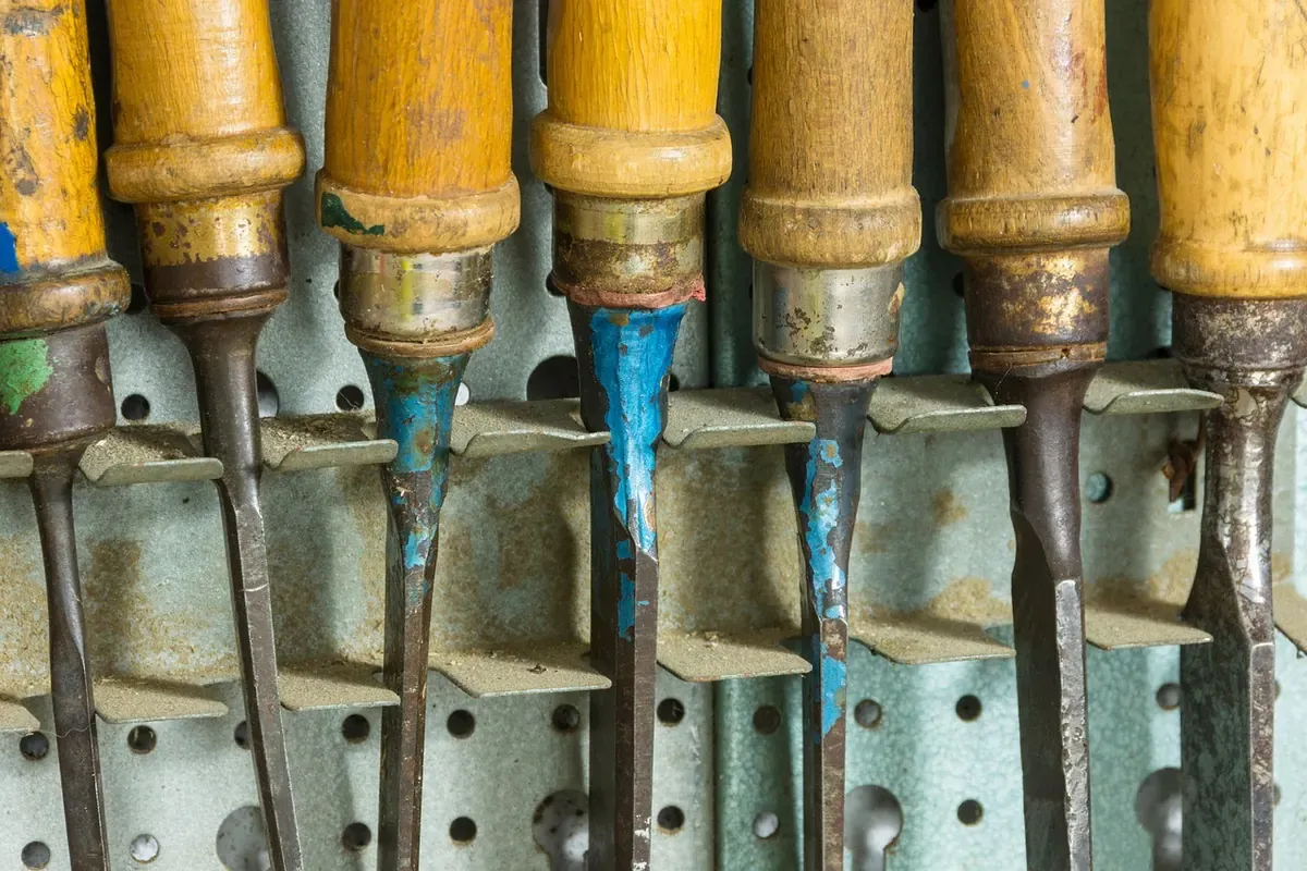 A row of wooden-handled chisels stored upright side by side in a rack.