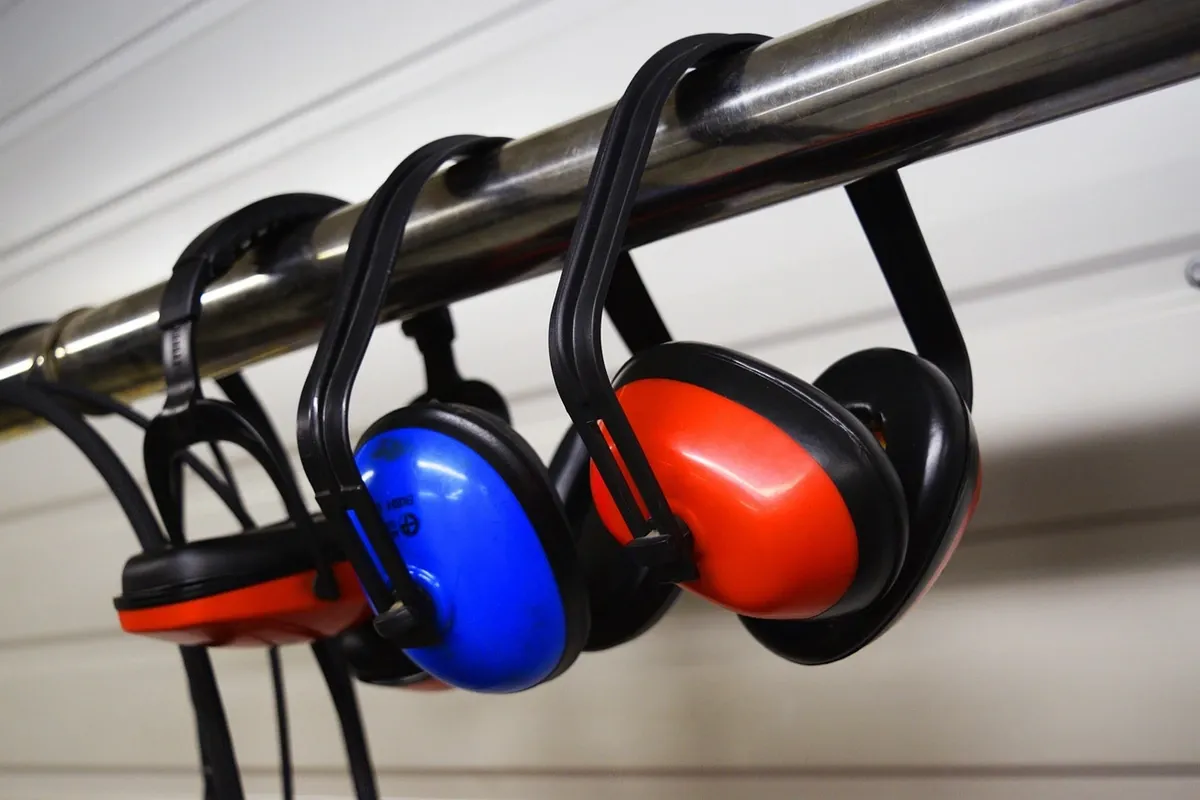 Two pairs of red and blue over-ear defenders hanging from a metal rail.