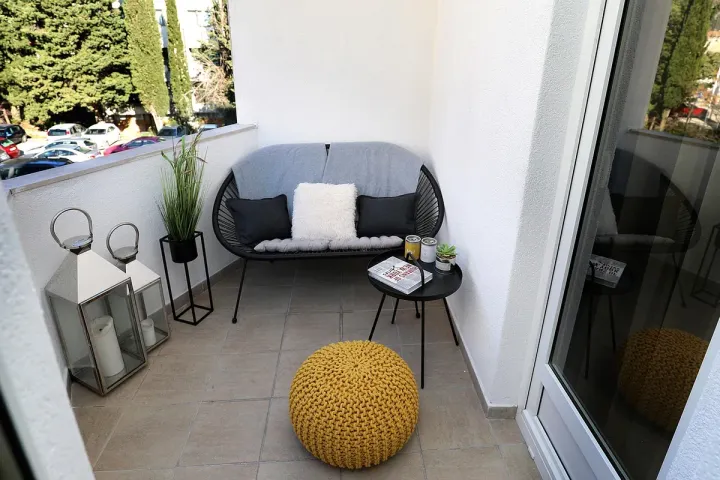 A small apartment balcony furnished with a compact sofa, lanterns and potted plants.