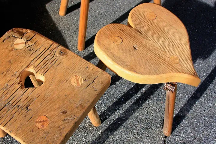 Two small solid wooden stools with shaped seats standing outdoors in daylight.